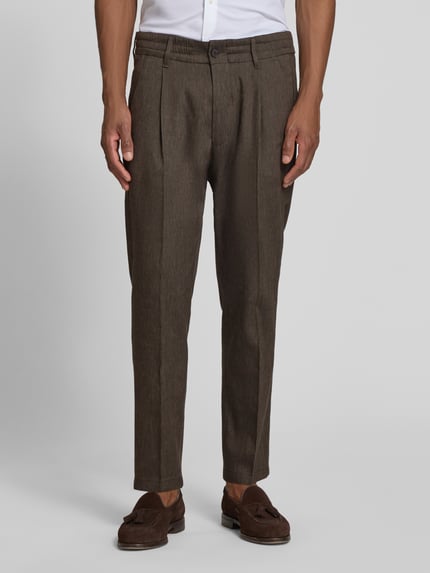Männermodel trägt Hose mit Bügelfalte und elastischem Bund Modell 'CHASY' von Drykorn, brauner Leinen-Mix mit Viskose-Anteil, Slim-Fit, Knopf- und Reißverschluss, französische Eingrifftaschen, klassische Gesäßtaschen, glatte Textur, Bundweite 44 cm, Innenbeinlänge 66 cm, Ganzkörperansicht von vorne.