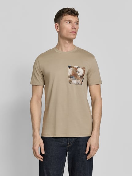 Männermodel trägt T-Shirt mit Brusttasche von ARMANI EXCHANGE in Beige, Reine Baumwolle, Gerader-Schnitt, Rundhalsausschnitt, Label-Detail, Ganzkörperansicht von vorne.