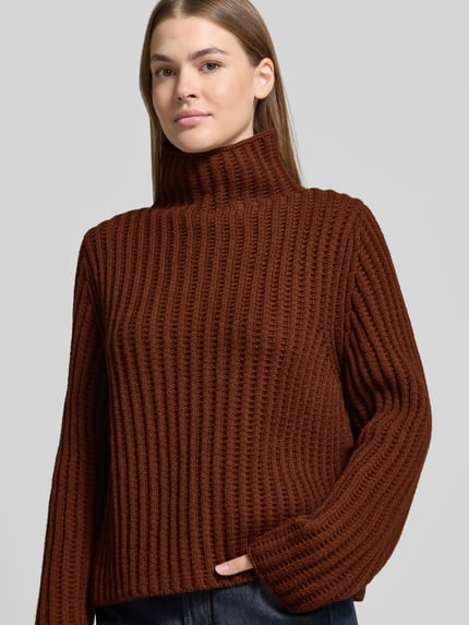 Frauenmodel trägt Strickpullover mit Stehkragen Modell 'ARWIE' von DRYKORN in Braun, grobe Rippstruktur, Material-Mix mit Alpaka, Regular Fit, Nahaufnahme Oberkörper.