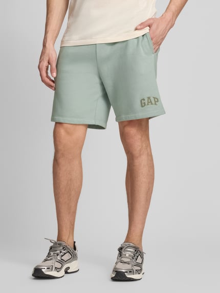 Männermodel trägt Sweatshorts mit Logo und elastischem Bund von GAP aus Baumwoll-Mix, Regular-Fit, Eingrifftaschen, mintgrün, Ganzkörperansicht von vorne.