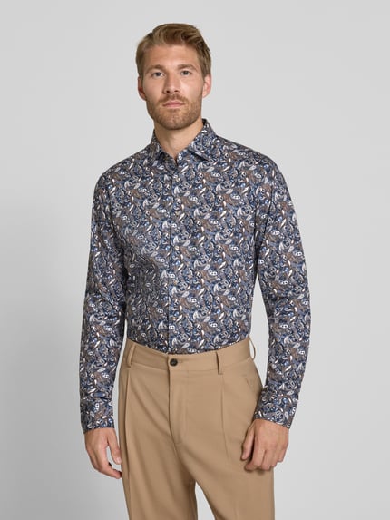 Männermodel trägt Businesshemd von Seidensticker mit blau-braunem Muster, beige Hose, Hintergrund einfarbig, Ganzkörperansicht von vorne. Herren Businesshemd von Seidensticker