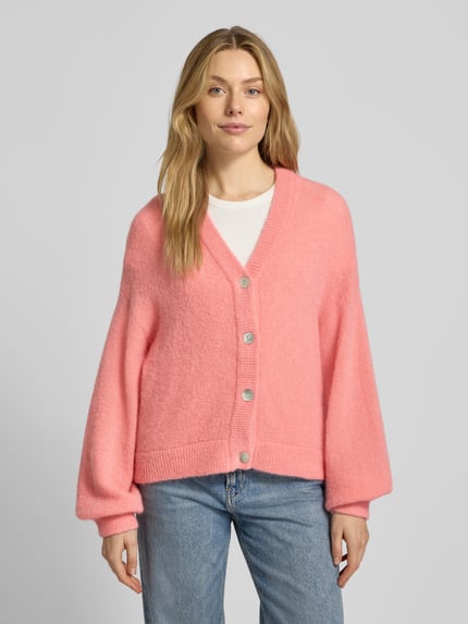 Frauenmodel trägt Strickjacke mit V-Ausschnitt Modell 'Petrinelle Hope' von MSCH Copenhagen in Rosa, lockerer Schnitt, Ganzkörperansicht von vorne. Material-Mix mit Alpaka, Knopfleiste, Ärmel und Rückenlänge passend für Größe S/M.