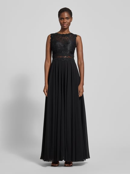 Frauenmodel trägt Abendkleid mit Spitze und Rundhalsausschnitt von Mascara, A-Linie, Maxikleid, Farbe Schwarz, detailreiche Textur am Oberteil, Rückenlänge bei Größe 36: 153 cm, Brustweite: 33 cm, Ganzkörperansicht von vorne.