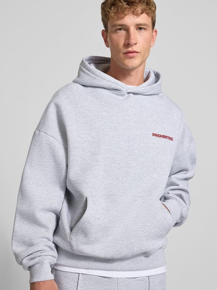 Männermodel trägt Relaxed Fit Hoodie aus Baumwoll-Mix mit Label-Detail von PROHIBITED in Hellgrau, Känguru-Tasche, Nahaufnahme Oberkörper.