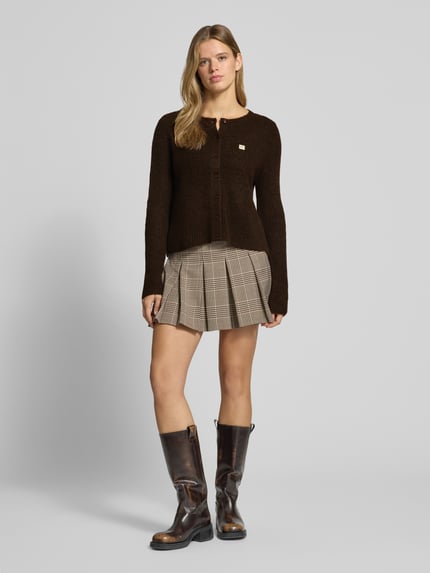 Frauenmodel trägt Cardigan mit Label-Patch von ONLY in unifarbener Strickoptik mit Knopfleiste, gerippten Abschlüssen, Ganzkörperansicht von vorne.