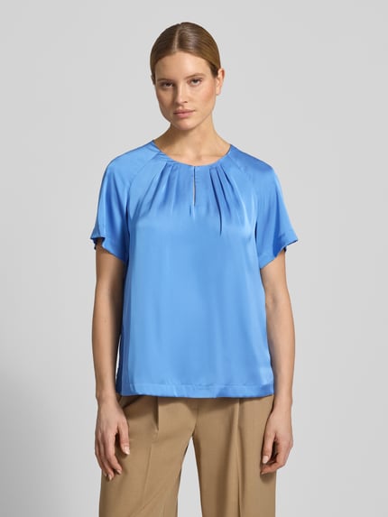 Frauenmodel trägt Blusenshirt aus Satin mit Rundhalsausschnitt von Comma in Blau mit Drapierungen, Regular-Fit, beige Hose, Ganzkörperansicht von vorne. Rückenlänge bei Größe 36: 60 cm, Ärmellänge bei Größe 36: 33 cm.