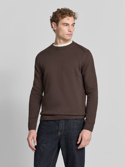 Männermodel trägt Pullover mit markanten Teilungsnähten von S.OLIVER CASUAL in unifarbenem Braun, Strickoptik, Struktur, Ganzkörperansicht von vorne.