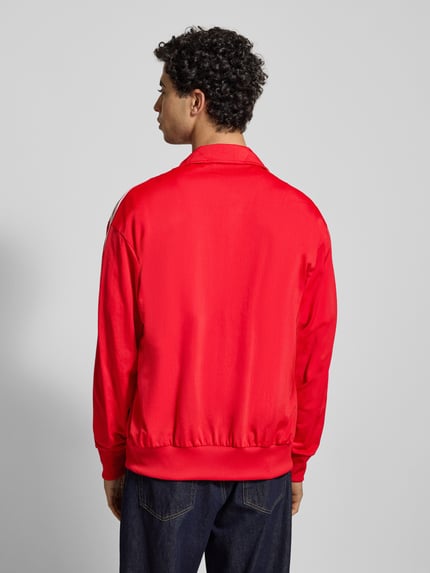 Männermodel trägt Sweatjacke mit Stehkragen von adidas Originals in kräftigem Rot, Regular-Fit, Material-Mix mit Stretch-Anteil, Rückenlänge 71 cm, Ärmel 65 cm, Reißverschluss, Label-Stitching, Reißverschlusstaschen, gerippte Abschlüsse, Ganzkörperansicht Rückansicht.
