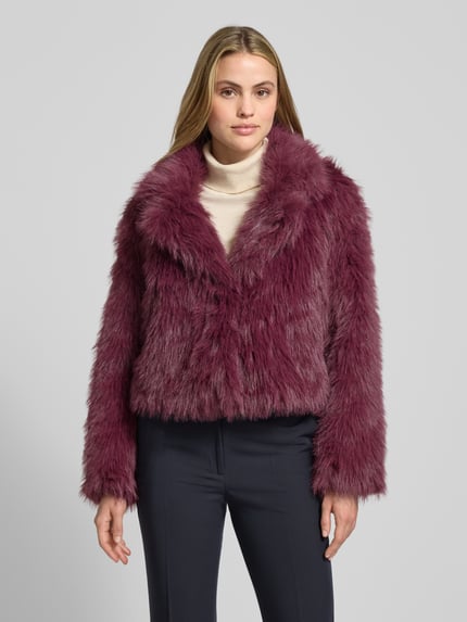 Vrouwenmodel draagt Regular Fit Jacke aus Teddyfell Modell 'NORA' van Vero Moda in effen bordeauxrood met staande kraag, lange mouwen en zijzakken, teddy textuur. Ganzkörperaanzicht van voren.