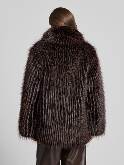 Frauenmodel trägt Jacke aus Kunstfell mit Schalkragen von PETITE M., dunkelbraune Töne, strukturierte Felloptik, Ganzkörperansicht Rückansicht. Rückenlänge 80 cm, Schulterbreite 49 cm, Brustweite 54 cm, Ärmellänge 68 cm, Regular Fit.