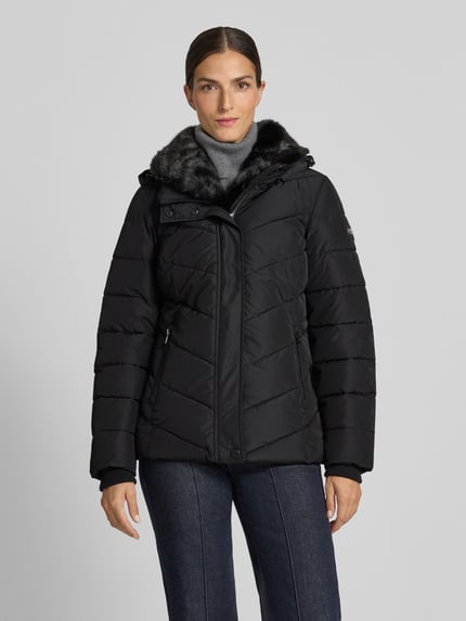 Frauenmodel trägt Regular Fit Jacke in Stepp-Optik von NAUTGÅRD in Schwarz mit Kunstfellbesatz und Eingrifftaschen, Ganzkörperansicht von vorne. Rückenlänge 68 cm, Schulterbreite 43 cm, Brustweite 47 cm, Ärmellänge 66 cm.