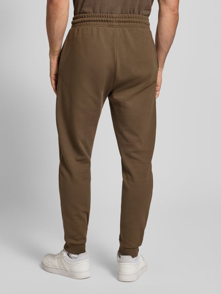 Męski model nosi Comfort Fit Sweatpants aus reiner Baumwolle Modell 'NAPIN' od Hugo Blue, jednolity brąz, elastyczny pas, tylna pełna sylwetka.