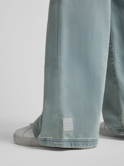 Frauenmodel trägt Wide Fit Jeans aus Baumwoll-Mix von Marc Cain in Hellblau mit sichtbarem Label, strukturierte Oberfläche, Nahaufnahme Bein. Damen Jeans von Marc Cain, elastischer Baumwoll-Mix, Wide Fit, elastischer Bund mit Tunnelzug, Eingrifftaschen, Bundweite bei Größe 36: 40 cm, Innenbeinlänge bei Größe 36: 83 cm.