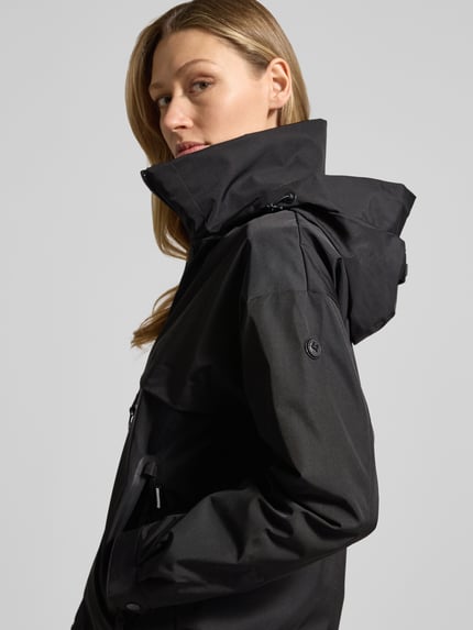 Modelka kobieca nosi Jacke mit Stehkragen von khujo, czarny kolor, krój regular fit, stójka, zamek, kieszenie na zamek, długość tyłu 60 cm, szerokość ramion 51 cm, szerokość w rozmiarze S 50 cm, długość rękawa 54 cm, ujęcie z przodu w półzbliżeniu