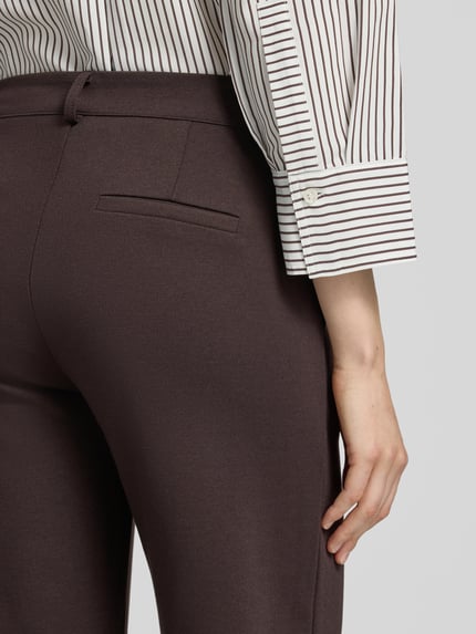Frauenmodel trägt Straight Fit Stoffhose mit Viskose-Anteil Modell 'Nanni' von FREE/QUENT, dunkelbraune Farbe, glatte Textur, Nahaufnahme Rückansicht. Elastischer Material-Mix, Haken- und Reißverschluss, Bundweite und Innenbeinlänge passend für Größe S.