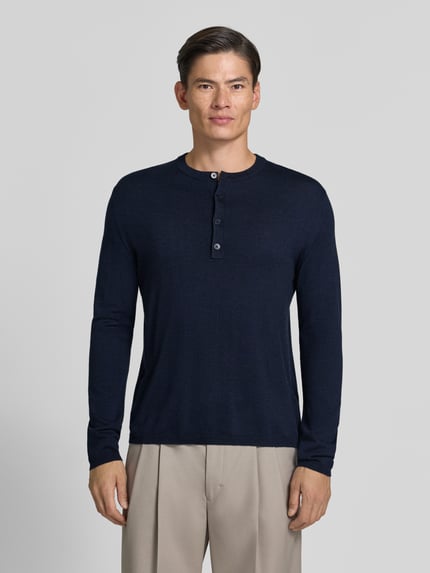 Männermodel trägt gebreide pullover mit Henley-kraag van DRYKORN, puur katoen, recht model, ribboorden, ruglengte maat L 70 cm, mouwlengte 71 cm, ganzlichaamsaanzicht van voren.