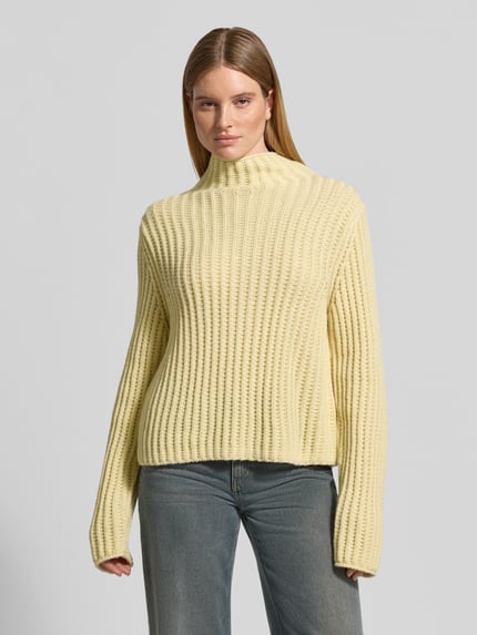 Frauenmodel trägt Strickpullover mit Stehkragen Modell 'ARWIE' von DRYKORN, beige, grob gerippte Textur, Regular Fit, Nahaufnahme Oberkörper. Material-Mix mit Alpaka-Anteil und langen Ärmeln, Rückenlänge 57 cm, Ärmellänge 63 cm.
