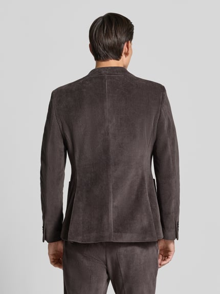 Männermodel trägt Slim Fit Sakko aus Baumwoll-Mix in Cord-Optik Modell 'Nick' von Zuitable in Braun, strukturierte Oberfläche, Ganzkörperansicht Rückansicht. Kontext: Elastischer Baumwoll-Mix, Reverskragen, Brusttasche, aufgesetzte Taschen, 2-Knopfleiste, Rückenlänge Größe 50: 72 cm, Schulterbreite: 45 cm, Ärmellänge: 67 cm.