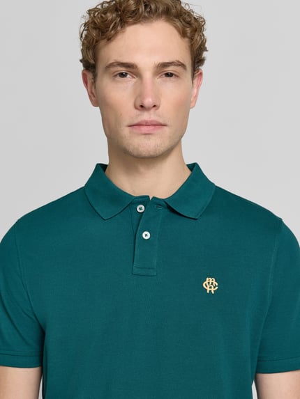 Męski model nosi Slim Fit Poloshirt mit Label-Stitching od MCNEAL z bawełny, krój slim fit, listwa guzikowa, długość tyłu 72 cm, zbliżenie na górną część ciała