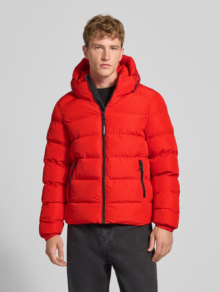 Männermodel trägt Steppjacke mit Label-Stitching und Kapuze von Superdry, leuchtend rot, schwarze Details, Ganzkörperansicht von vorne. Herren Steppjacke, gerader Schnitt, Kapuze mit Kordelzug, Reißverschluss, seitliche Eingrifftaschen, elastische Ärmelabschlüsse.