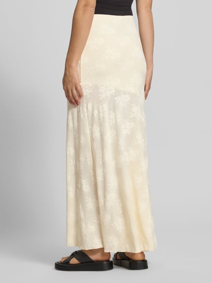Frauenmodel trägt Maxirock mit elastischem Bund von Gina Tricot, Material-Mix mit Stretch-Anteil, Gerader-Schnitt, Embroidery Design, sanfte Cremefarbe, florale Textur, Damen, Ganzkörperansicht Rückansicht.