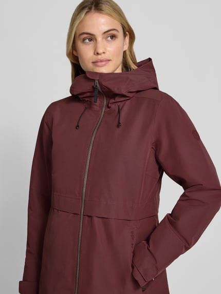 Frauenmodel trägt Regular Fit Parka mit Kapuze von Didriksons in dunklem Rot, glatte Textur, Zweiwege-Reißverschluss, Nahaufnahme Oberkörper. Rückenlänge 87 cm, Schulterbreite 41 cm, Brustweite 48 cm, Ärmellänge 55 cm.