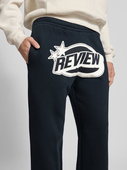 Frauenmodel trägt Straight Leg Sweatpants mit Logo und elastischem Bund von Review aus Baumwoll-Mix, Logo vorne, Nahaufnahme Oberkörper.