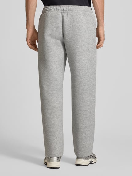 Männermodel trägt Regular Fit Sweatpants aus Material-Mix Modell 'BILL LEGACY' von JACK & JONES in Hellgrau, elastischer Bund, Ganzkörperansicht Rückansicht, Herren Sweatpants, Eingrifftaschen, 77 cm Innenbeinlänge, KI-modifiziertes Bild.