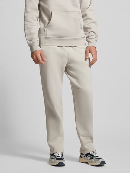 Männermodel trägt Straight Fit Sweatpants mit Label-Stitching von CHAMPION aus Baumwoll-Mix, elastischer Bund, cremefarben, Ganzkörperansicht von vorne.