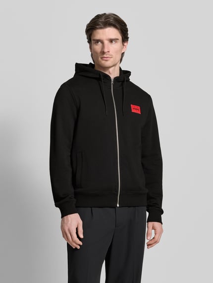 Männermodel trägt schwarze Sweatjacke aus Baumwolle Modell 'Daple212' von HUGO mit Kapuze, Reißverschluss, Label-Patch, Nahaufnahme Oberkörper.