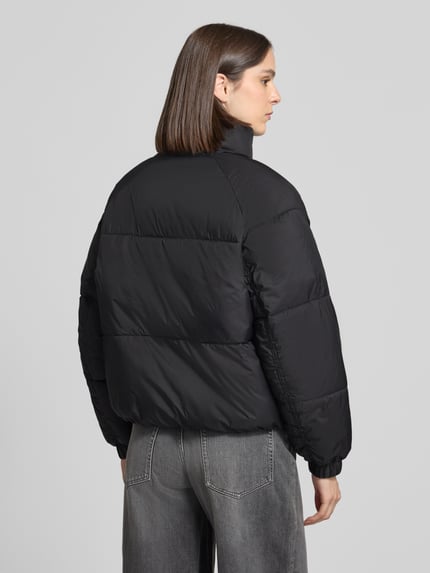Frauenmodel trägt schwarze, unifarbene Pufferjacke mit Stehkragen Modell 'VMBRENDA' von VERO MODA, Steppeinsatz, Rückansicht Ganzkörperansicht.
