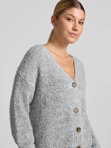 Frauenmodel trägt Cardigan mit V-Ausschnitt Modell 'So44fia' von ZABAIONE aus grauem Material-Mix, Knopfleiste, Nahaufnahme Oberkörper. Material-Mix mit Viskose-Anteil, gerader Schnitt, Rückenlänge 56 cm, Ärmellänge 47 cm.