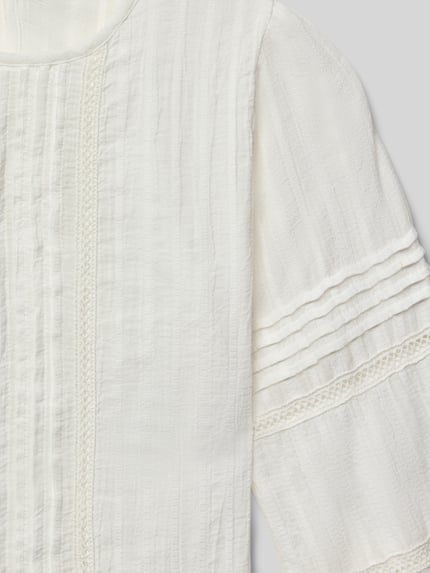 Mädchen trägt Blusenshirt mit Rundhalsausschnitt von Mango aus reiner Baumwolle, lockerer Schnitt, Raffungen, Nahaufnahme Oberkörper.