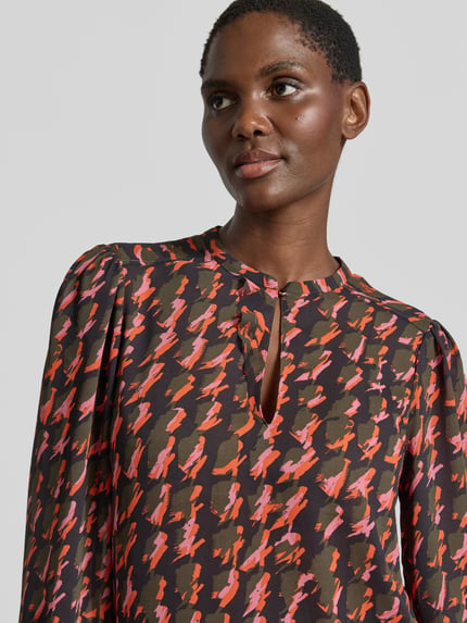 Frauenmodel trägt Regular Fit Bluse im Allover-Look mit Schlüsselloch-Ausschnitt von Marc Cain, Chiffon, Muster in Braun, Rot und Rosa, Nahaufnahme Oberkörper.