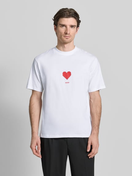 Männermodel trägt Regular Fit T-Shirt aus reiner Baumwolle Modell 'DALENTIN' von HUGO in Weiß mit rotem Motiv-Print, ganzkörperansicht von vorne.