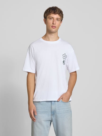 Männermodel trägt Relaxed Fit T-Shirt aus reiner Baumwolle Modell "DYLAN" von JACK & JONES in Weiß mit Print-Detail, Nahaufnahme Oberkörper.