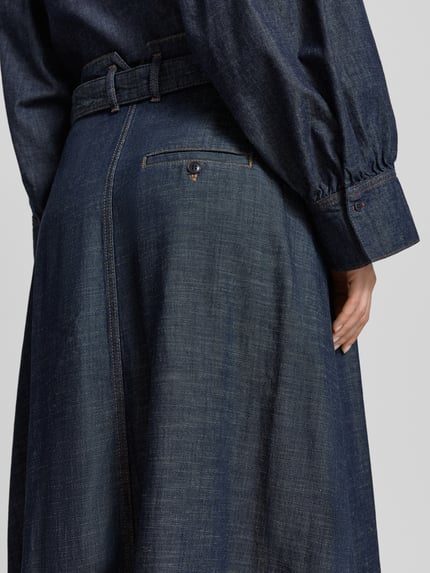 Frauenmodel trägt Jeansrock aus Lyocell-Mix mit Bindegürtel Modell 'EDMEA' von Drykorn, dunkelblaue Farbstruktur, Nahaufnahme Rückansicht, Damen, Lyocell-Mix, Gerader-Schnitt, Midirock, Bundweite bei Größe 27: 37 cm, Gesamtlänge bei Größe 27: 89 cm.