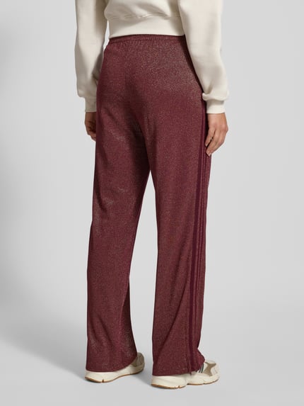 Vrouwenmodel draagt Sweatpants met elastische tailleband van adidas Originals, bordeauxrood, glittereffect, katoenmix, losse pasvorm, ritszakken, labelstiksel, volledige lichaamsweergave van achteren.