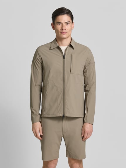 Männermodel trägt Regular Fit Jacke mit Umlegekragen Modell 'Motion' von SCANDINAVIAN EDITION in Beige, glatte Textur, Ganzkörperansicht von vorne. Elastischer Material-Mix, Napoleontasche, Zweiwege-Reißverschluss, Eingrifftaschen, Maße Größe M.