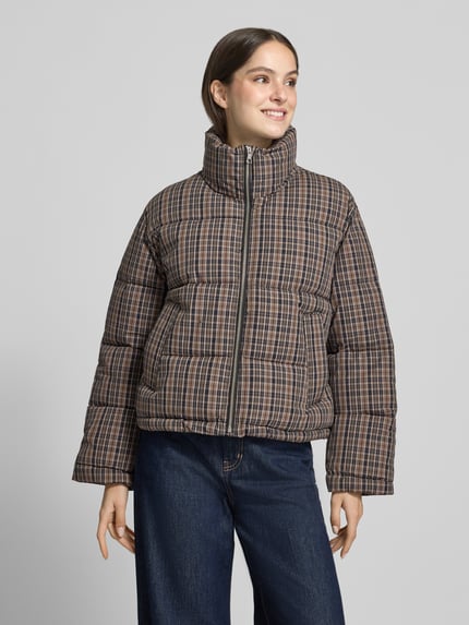 Frauenmodel trägt Steppjacke mit Stehkragen Modell 'LAURI' von MANGO im Allover-Karomuster, Reißverschluss, Eingrifftaschen, Ganzkörperansicht von vorne.
