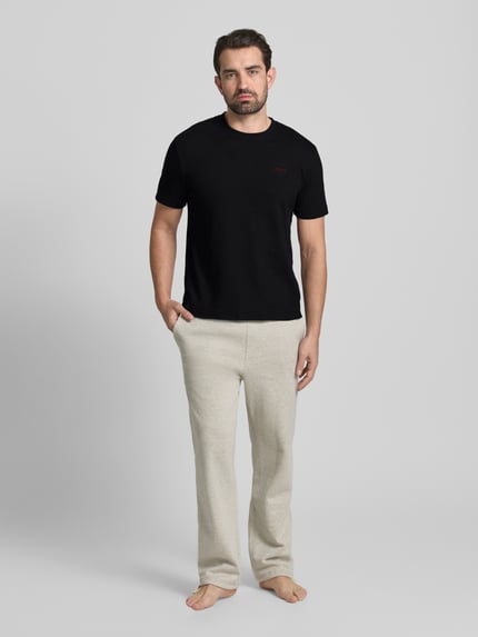Męski model nosi T-shirt mit Label-Stitching Modell 'Austin' von HUGO z mieszanki bawełny, krój regular fit, okrągły dekolt, długość tyłu w rozmiarze M: 69 cm, czarny, gładka faktura, Ganzkörperansicht von vorne.