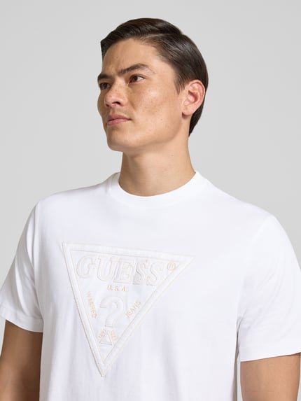 Männermodel trägt T-Shirt mit Logo und Rundhalsausschnitt von Guess aus reiner Baumwolle, Regular-Fit, Logo, Rückenlänge 70 cm, Nahaufnahme Oberkörper.