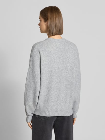 Frauenmodel trägt Strickpullover mit Label-Print von REVIEW in Hellgrau, lockerer Schnitt, gerippter Saum, Ganzkörperansicht Rückansicht.