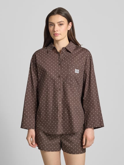 Frauenmodel trägt Relaxed Fit Bluse im Allover-Look Modell 'FRIDA' von Noisy May, Braun mit weißen Punkten, Material-Mix, Hemdblusenkragen, Brusttasche, Label-Detail, Rückenlänge 76 cm, Ärmellänge 52 cm, Ganzkörperansicht von vorne.