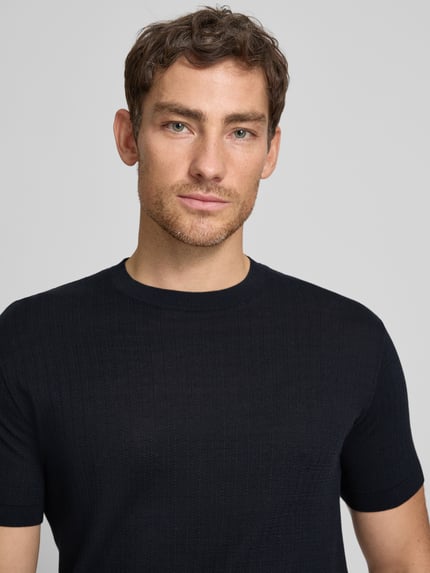 Mannenmodel draagt gebreid shirt met ronde hals van ARMANI EXCHANGE, puur katoen, slim fit, ruglengte bij maat M 69 cm, detailopname bovenlichaam.