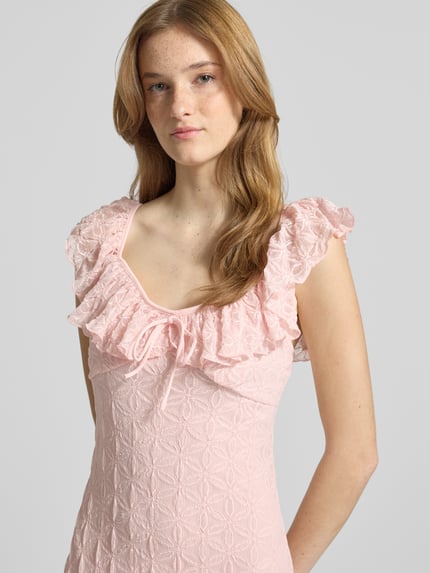 Vrouwenmodel draagt Midikleid met Spitze und Schleifen-Detail van Gina Tricot in lichtroze materiaalmix met stretch, nauwsluitend model, hartvormige hals, volants, borstwijdte maat S 32 cm, ruglengte 117 cm, nahaufnahme bovenlichaam.