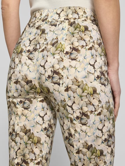 Frauenmodel trägt Stoffhose aus Viskose-Mix Modell 'Fimi' von STEHMANN mit floralem Muster, Label-Detail, Nahaufnahme Rückansicht. Damen Stoffhose aus Viskose-Elasthan-Mix mit körpernaher Passform, elastischem Bund, verkürzte Passform, Bundweite 39 cm, Innenbeinlänge 69 cm, Größe 36.