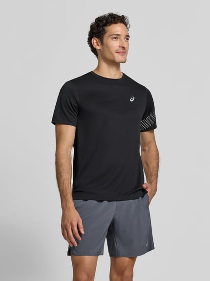 Männermodel trägt Regular Fit T-shirt mit labelprint Model 'ICON' van ASICS TIGER, zwarte kleur, ronde hals, ruglengte maat M 71 cm, ganzkörperansicht van voren.