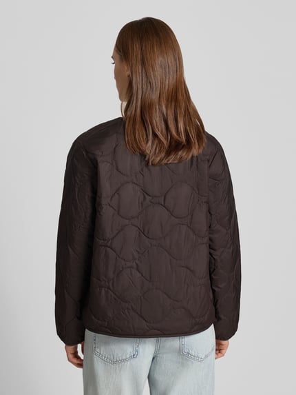 Frauenmodel trägt Steppjacke mit Logo-Stitching Modell 'Skye' von Carhartt Work In Progress in Dunkelbraun, strukturierte Oberfläche, Ganzkörperansicht Rückansicht. Gerader Schnitt, Rundhalsausschnitt, Rückenlänge 60 cm, Schulterbreite 42 cm, Brustweite 53 cm, Ärmellänge 62 cm.