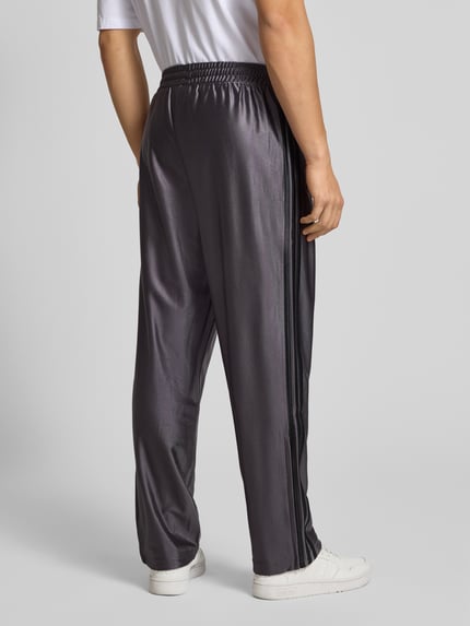 Männermodel draagt Jogpants mit Label-Stitching Modell 'FIREBIRD' van adidas Originals in grijs, regular fit, elastische tailleband, Ganzkörperansicht Rückansicht.